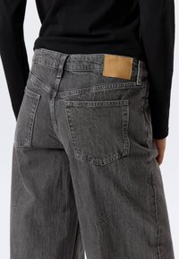 Grau-graue Jeans aus Denim zeichnen sich durch eine lässige Passform, sichtbare Nähte, zwei Gesäßtaschen und ein hellbraunes Lederetikett mit der Aufschrift "WEEKDAY" aus.