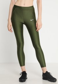 Dopasowane legginsy w oliwkowym kolorze o gładkiej fakturze, z kontrastowym brązowym przeszyciem i małym białym logo Nike na udzie.