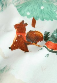Bawełniana tkanina z ilustracją brązowej wiewiórki w czerwonym szaliku, otoczona zielonymi drzewami i płatkami śniegu, charakteryzuje się miękką fakturą.