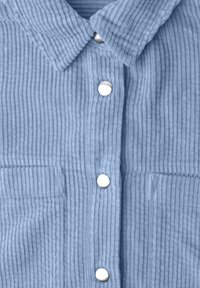 Light blue corduroy shirt with a collar, four silver snap buttons down the front, and two front pockets.