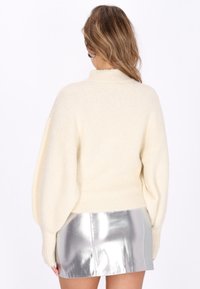 Pull oversized couleur crème avec un col montant, des poignets côtelés et une texture douce et moelleuse. Associe avec une mini-jupe en argent brillant.