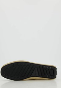 Beige Wildlederschuh mit einer strukturierten schwarzen Gummisohle, die über ein gemustertes Profil und ein Logo an der Seite verfügt.