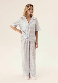 Jasnoniebieski i biały pijama w kratkę z krótkim rękawem, koszulą zapinaną na guziki oraz luźnymi spodniami. Na nogach białe sneakersy.
