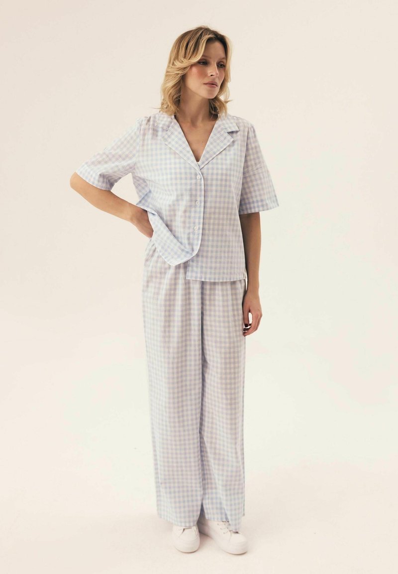 Jasnoniebieski i biały pijama w kratkę z krótkim rękawem, koszulą zapinaną na guziki oraz luźnymi spodniami. Na nogach białe sneakersy.