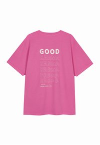 Camiseta de algodón rosa con un gráfico en la parte posterior en blanco que presenta el texto "BUENA KARMA" en diferentes fuentes y tamaños, con "ÚNETE A NUESTRO CLUB DE BUENA KARMA" abajo.