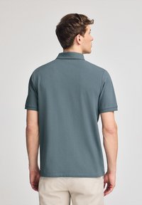 Camisa polo de suave tejido gris, con un cuello clásico y mangas cortas, con un dobladillo recto y un diseño minimalista.
