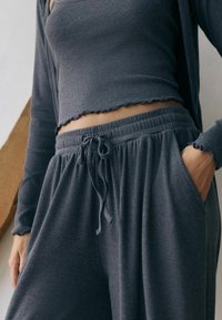 Gray ribbed crop top with scalloped edges paired with drawstring lounge pants featuring side pockets, all made from soft, textured fabric.