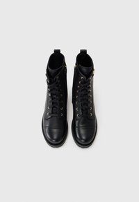 Black leather ankle boots with gold eyelets, front lacing, and side zippers. Smooth texture and rounded toe design.