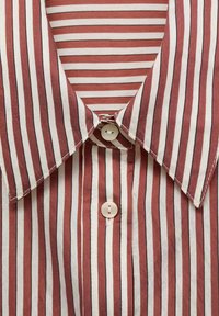 Striped shirt featuring red and white vertical stripes, a pointed collar, and a light button at the neckline, made of a soft fabric.