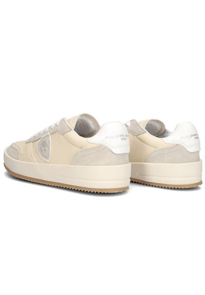 Beige sneakers med en glat læder- og ruskindsoverflade, der har en kraftig sål, hvide accenter og et logo-patch på siden.