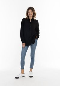Zwarte lange mouwen overhemd met kraag, gedragen met lichtblauwe skinny jeans en witte sneakers, met een ontspannen pasvorm en zachte textuur.