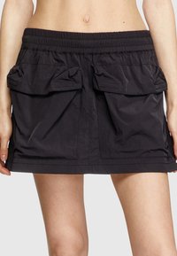Gonna nera realizzata in tessuto leggero con vita elastica, dotata di due ampie tasche frontali e un design leggermente svasato.