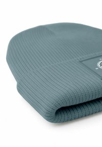 A folded beanie hat in soft, ribbed fabric, featuring a muted teal color and a small logo patch on one side.
