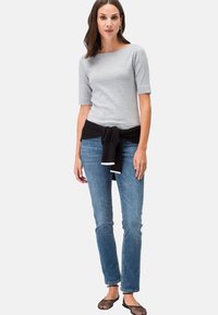 Graues Kurzarmoberteil mit einem schwarzen Taillengürtel, kombiniert mit hellblauen geraden Jeans und schwarzen strukturierten Ballerinas. Minimalistisches Design.
