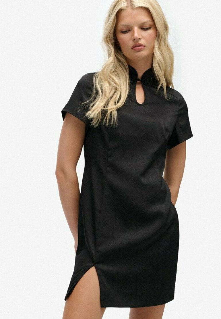 Schwarzes Kleid mit kurzen Ärmeln, Schlüsselloch-Ausschnitt und seitlichem Schlitz. Hergestellt aus glattem Stoff mit figurbetontem Design und nahtloser Verarbeitung.