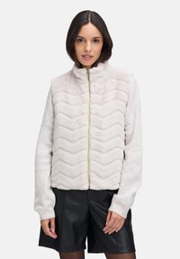 Helle rosa, zip-up Jacke aus weichem, strukturiertem Stoff mit einem Zickzackmuster; ausgestattet mit einem hohen Kragen und gerippten Ärmeln.