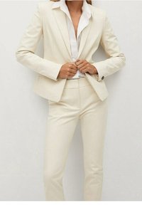 Completo su misura color crema con giacca strutturata e pantaloni slim-fit coordinati, con una camicia bianca sotto.
