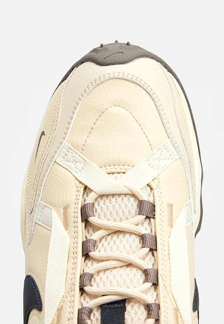 Kremowe sneakersy z skórzaną cholewką, siateczkowym językiem, brązowymi sznurowadłami i ciemnymi akcentami. Posiadają teksturowane panele oraz zaokrąglony czubek.