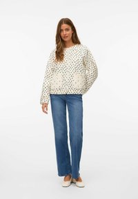 Gequilted crèmekleurige jas met een blauw bloemenpatroon, ritssluiting en zijzakken; gecombineerd met lichtblauwe rechte jeans en platte schoenen.