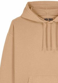 Sweatshirt à capuche beige en tissu doux, avec une poche avant, des poignets côtelés et une étiquette logo à l'intérieur du col.
