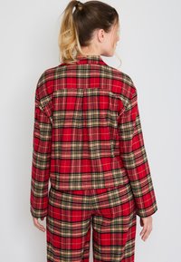 Rode en zwarte geruite flanellen loungewear set met een blouse met kraag en bijpassende broek, gemaakt van een zachte, gestructureerde stof.