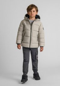 Ljusgrå puffjacka med huva, svart dragkedja och sidofickor. Buren �över en grå tröja med mörkgrå cargo-byxor och svarta sneakers.