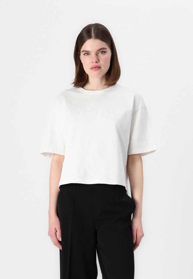 Tricou alb scurt, din material moale, cu decolteu rotund și mâneci scurte, având detalii cu cusături texturate și o croială lejeră.