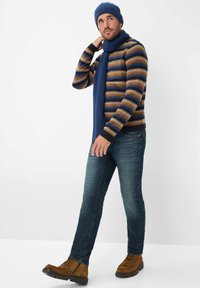 Gebreide gestreepte trui in bruin, blauw en beige; bijpassende blauwe geribde sjaal en muts. Draag met blauwe spijkerbroeken en bruine schoenen.