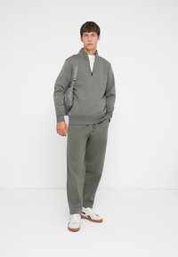 Grauer Kapuzenpulli mit einem Halb-Reißverschluss-Kragen, passenden Jogginghosen und weißen Sneakers. Der Stoff wirkt glatt und hat eine lockere Passform.