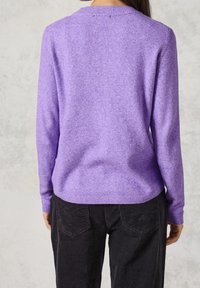 Maglione viola con una texture morbida, scollatura rotonda e maniche lunghe. Abbinato a pantaloni in corduroy neri con dettagli sulle tasche.