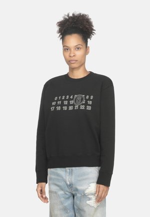Felpa nera con colletto rotondo, numeri grafici e un design circolare stampato in bianco sul davanti, abbinata a jeans chiari strappati.