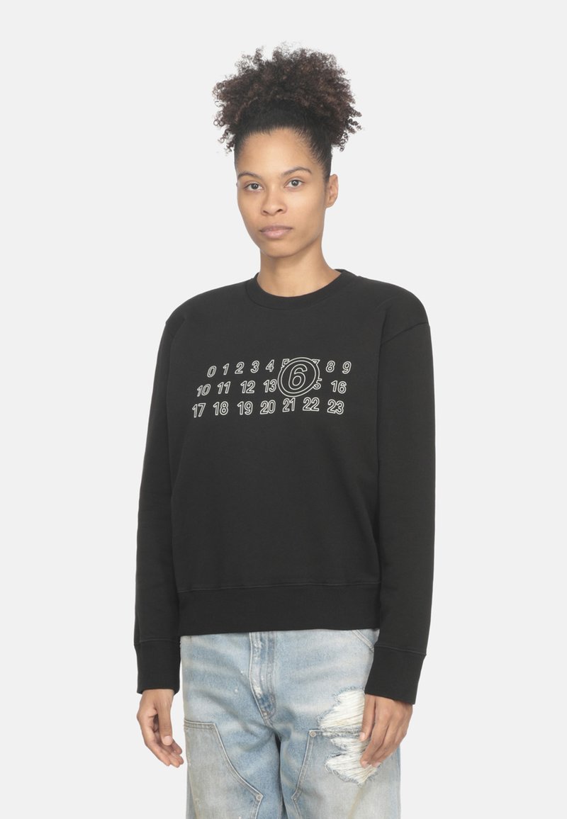 Felpa nera con colletto rotondo, numeri grafici e un design circolare stampato in bianco sul davanti, abbinata a jeans chiari strappati.