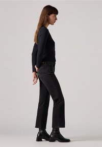 Zwarte lange mouw top gecombineerd met donkere denim jeans, met een slim fit die uitloopt bij de enkel. Draag het met zwarte enkellaarsjes.