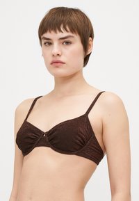 Soutien-gorge de bain métallisé marron foncé avec des détails froncés, des bretelles fines ajustables et un accent en torsion central. Texture douce, design à couverture minimale.