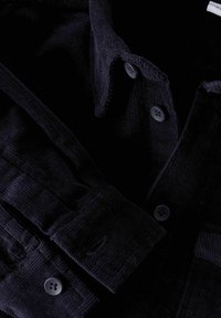 Granatowa koszula z sztruksu z kołnierzykiem zapinanym na guziki i teksturowanym materiałem. Dwa guziki widoczne na mankiecie i zapięciu z przodu.