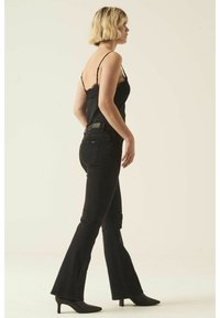 Un jean flare noir associé à un débardeur noir avec une bordure en dentelle. Les jeans ont une taille mi-haute et des poches arrière discrètes. Des talons aiguilles noirs.