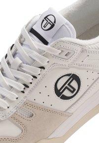 Biela teniska s čierno-bielym kruhovým logom, bielymi šnúrkami, béžovými semišovými detailmi a perforovanou bočnou časťou.