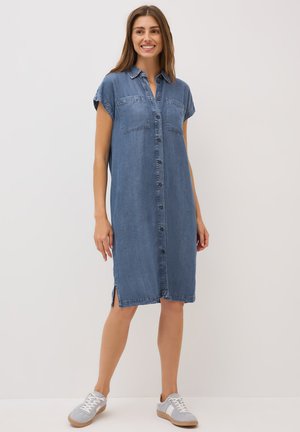 Denim skjortekjole med korte ærmer, knaplukning foran, to brystlommer, sidesplit og en lys blå farve. Båret med grå sneakers.