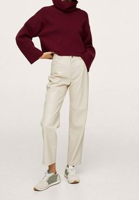 Burgunderfarbener Rollkragenpullover mit einem verkürzten Design, beige hoch taillierte Hose und weiße Sneakers mit grünen Akzenten und strukturierten Details.