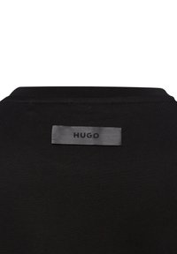 Zwarte t-shirt met een gladde, zachte textuur; heeft een grijs label met "HUGO" gestikt op de achterkant nabij de halslijn.