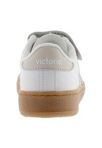Zapatilla blanca de cuero con una correa de velcro gris, suela de goma texturizada y logo "victoria" en el talón. Diseño atlético clásico.