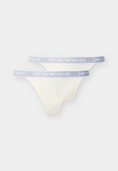 Δύο λευκά εσώρουχα τύπου στρινγκ με γκρι ελαστικές ζώνες στη μέση που φέρουν το λογότυπο "Emporio Armani" σε λευκά γράμματα.