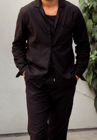 Czarna lniana marynarka z jedną kieszenią, sparowana z dopasowanymi spodniami. Luźny krój z lekko teksturowaną powierzchnią, ręce w kieszeniach.