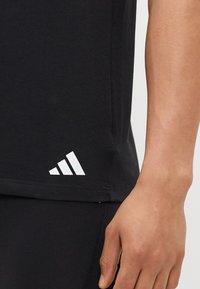 Schwarzes Sport-T-Shirt aus Baumwolle mit einem weißen Drei-Streifen-Logo in der unteren linken Ecke und einem klassischen Rundhalsausschnitt.