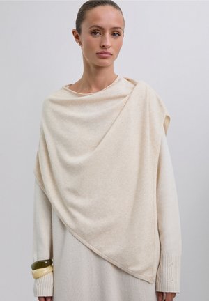 Poncho grande color beige claro hecho de tela suave, cayendo elegantemente. Incluye mangas texturizadas con un patrón de canalé y detalles decorativos.