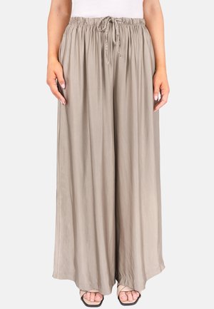 Hell taubefarbene, weit geschnittene Hose mit elastischem Kordelzug in der Taille, getragen von einer Person, die mit sichtbaren Händen und Füßen in Sandalen steht.