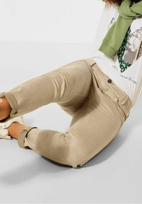 Beige cotton trousers with a slim fit, rolled cuffs, and a subtle sheen. Features front pockets and a button closure with a zip fly.
