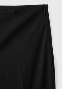Tissu de jupe noire avec une fermeture éclair fermée sur le bord supérieur droit, présenté sur un fond gris clair.