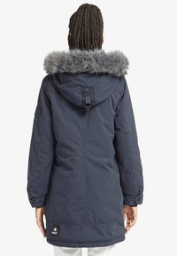 Navy parka with fur-trimmed hood, featuring a buttoned cuff and adjustable back strap. Displaying a patch logo near the hem.