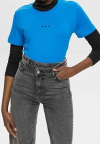 Lysblå kortærmet t-shirt med tre sorte hjertegrafikker på brystet, parret med højtaljede sorte denimjeans.